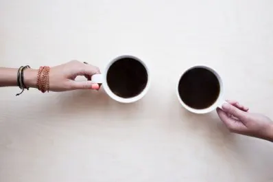 two different hands picking up a cup of coffee - arial view